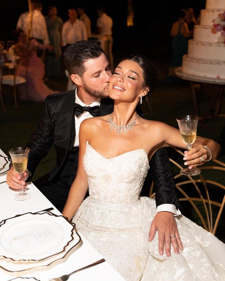 Пара с бокалами за столом, жених целует невесту в щёку